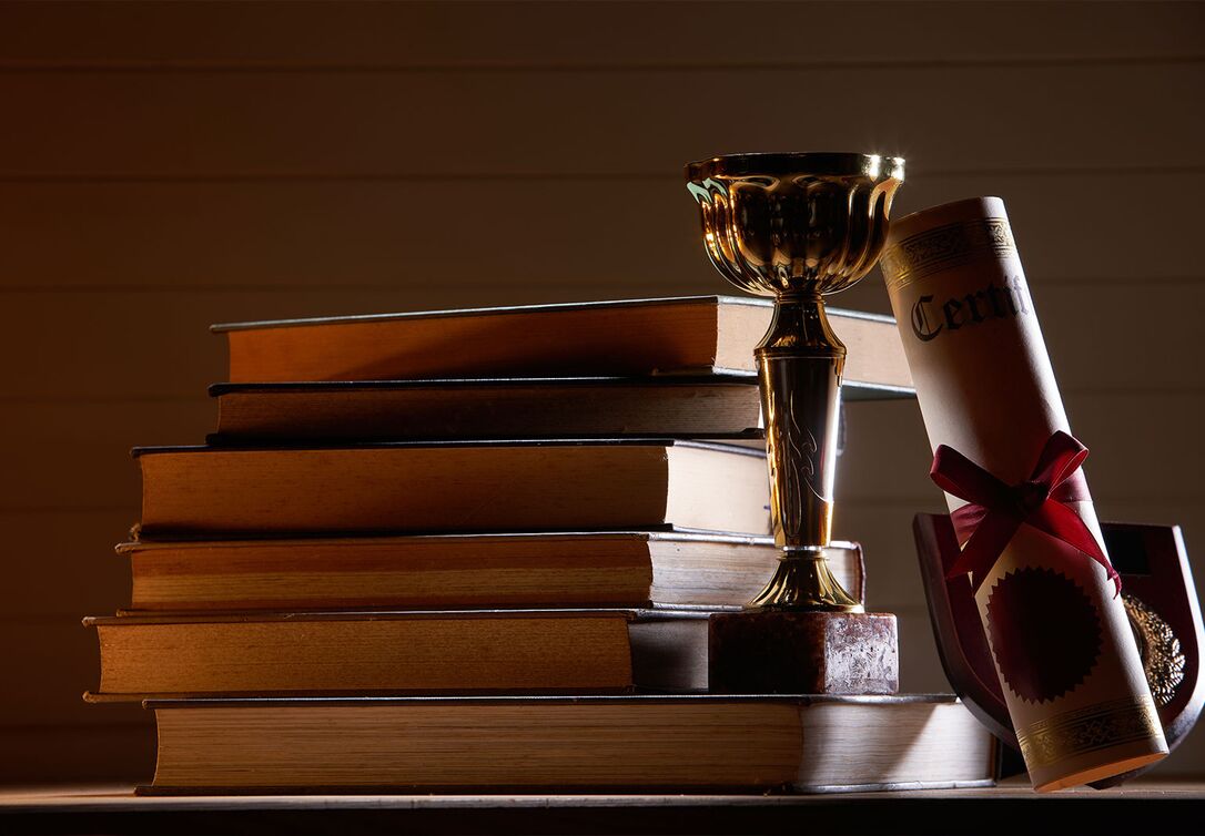 Gestapeltes Bücherregal mit goldener Trophäe, gerolltem Zertifikat und Auszeichnungstafel